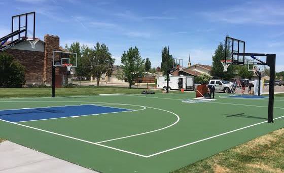Outdoor basketball court with green surface, blue key and multiple hoops in a residential neighborhood