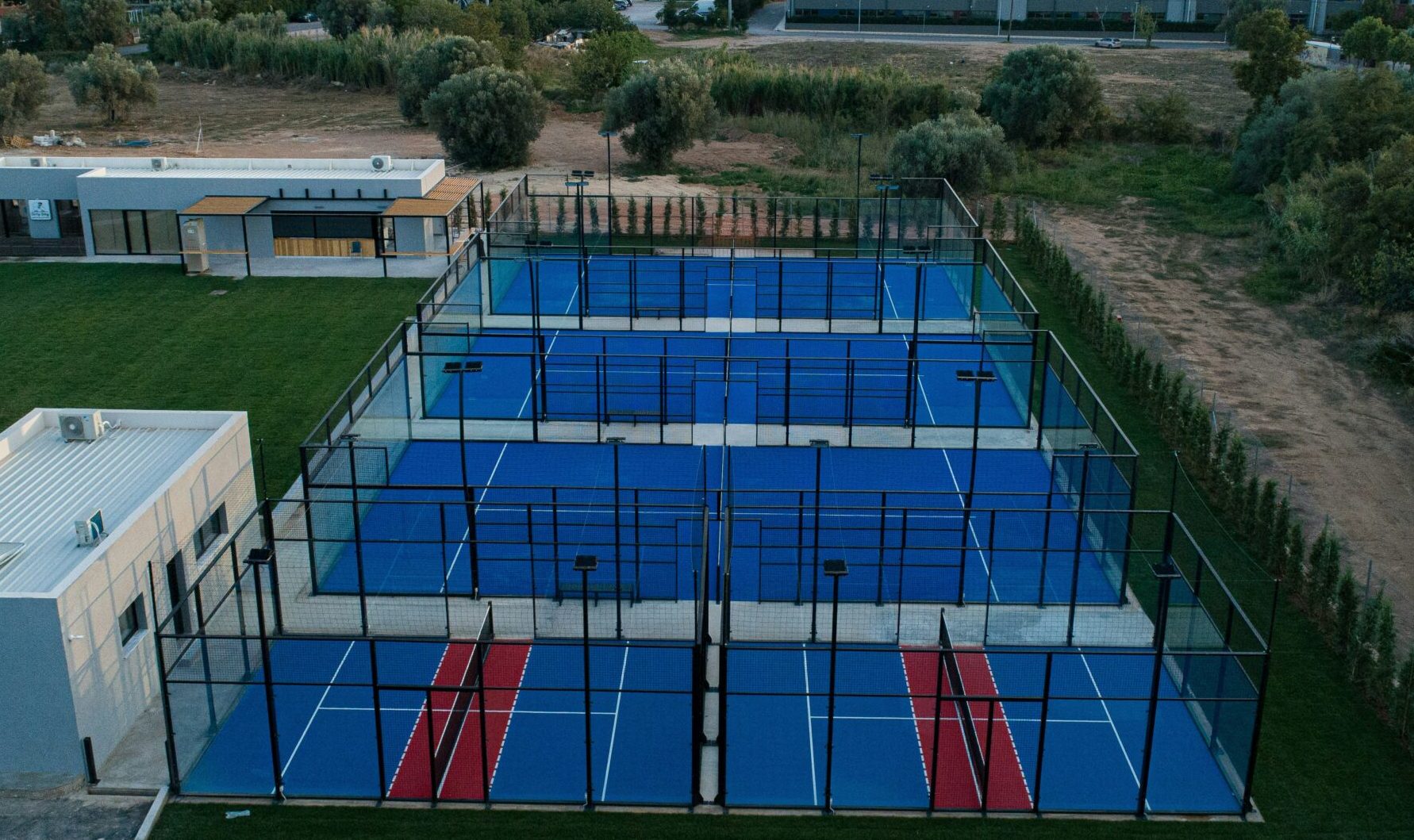 Enclosed padel courts with blue surfaces, glass back walls and black steel framing