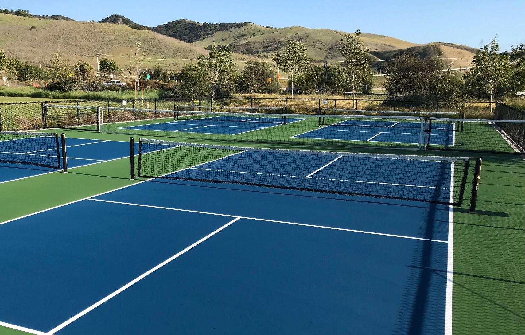 Backyard pickleball court with blue playing area, green surround and black fencing in Utah County