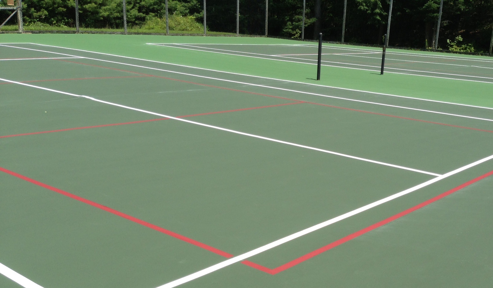 Freshly surfaced green tennis court with white and red laser-set lines and black fencing in Utah County